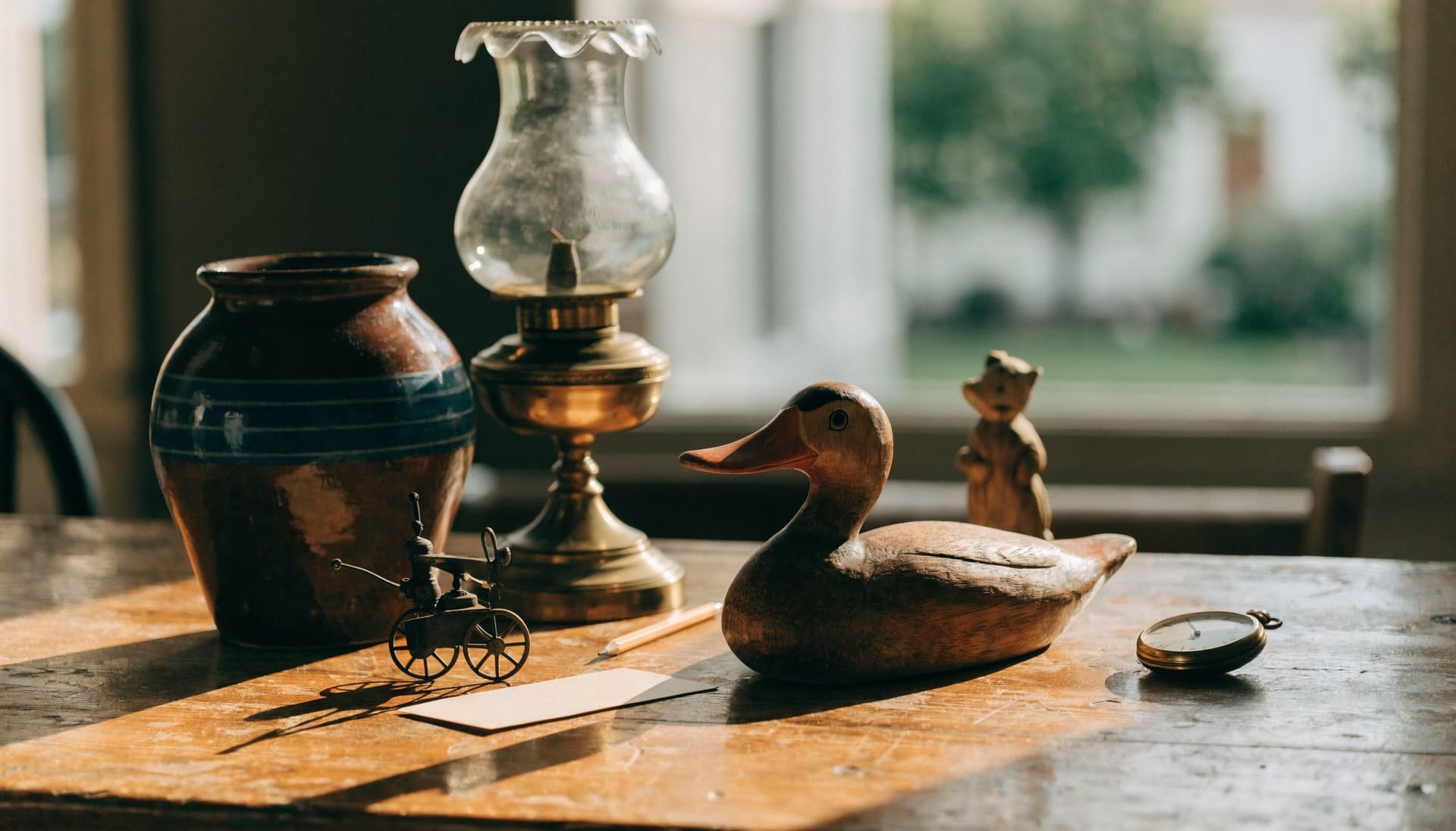 Representative photograph: a carved duck decoy, stoneware crock, brass oil lamp, tin toy and pocket watch being catalogued on a pine harvest table